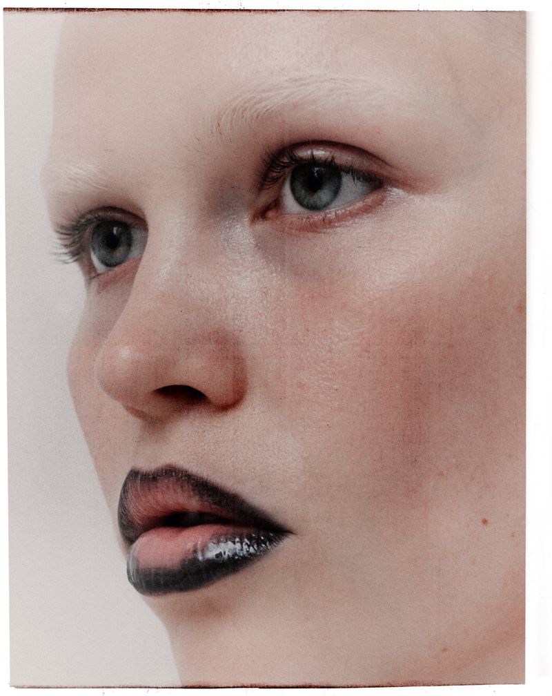 Close-up portrait of model Roos Schreiner with dark outlined lips and pale blonde eyebrows against a neutral background.