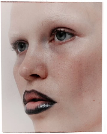 Close-up portrait of model Roos Schreiner with dark outlined lips and pale blonde eyebrows against a neutral background.