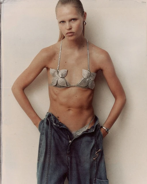 Model Roos Schreiner wearing a rhinestone bra and denim trousers against a plain wall for WRPD Magazine.