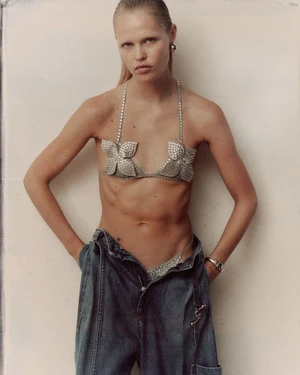 Model Roos Schreiner wearing a rhinestone bra and denim trousers against a plain wall for WRPD Magazine.