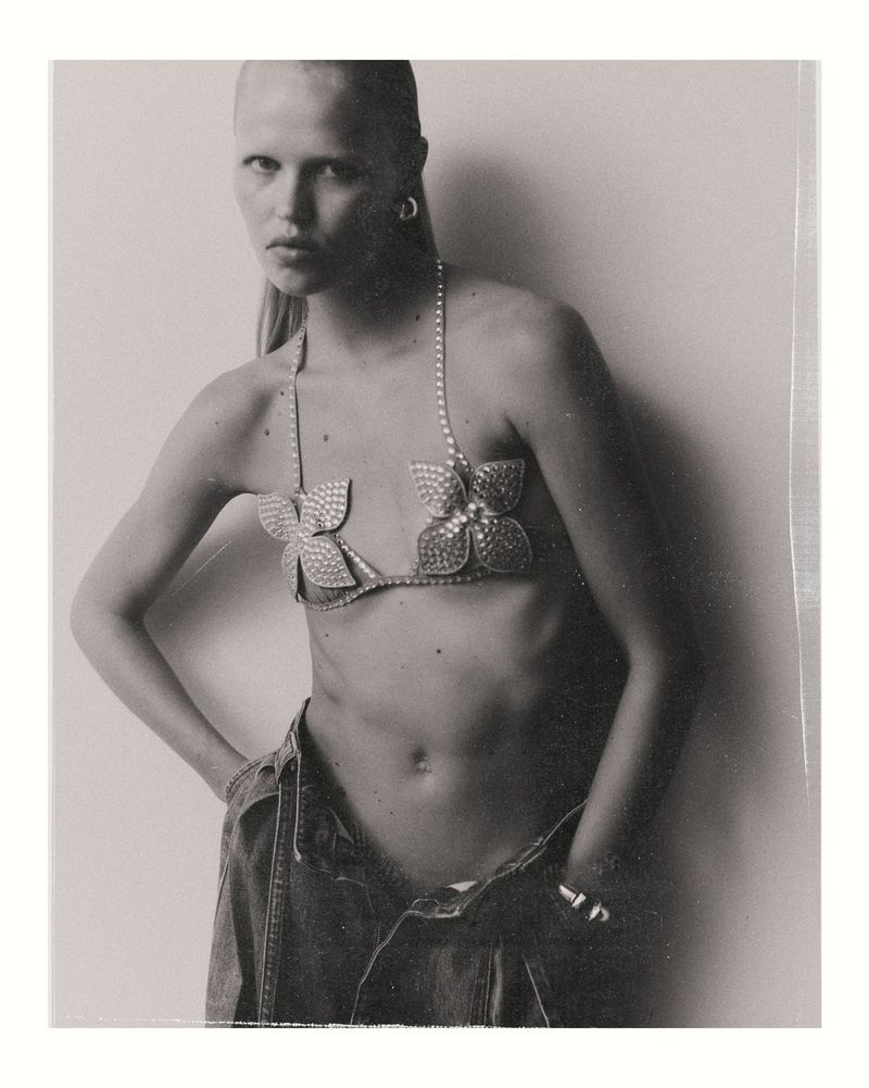 Model wearing a rhinestone flower bra and low-rise denim jeans against a plain white background