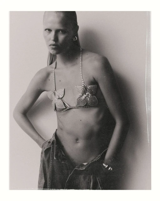 Model wearing a rhinestone flower bra and low-rise denim jeans against a plain white background