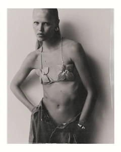Model wearing a rhinestone flower bra and low-rise denim jeans against a plain white background