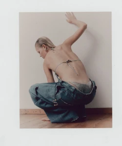 Model squatting against a white wall wearing low-slung denim cargo pants and a sparkling bikini top for WRPD Magazine.