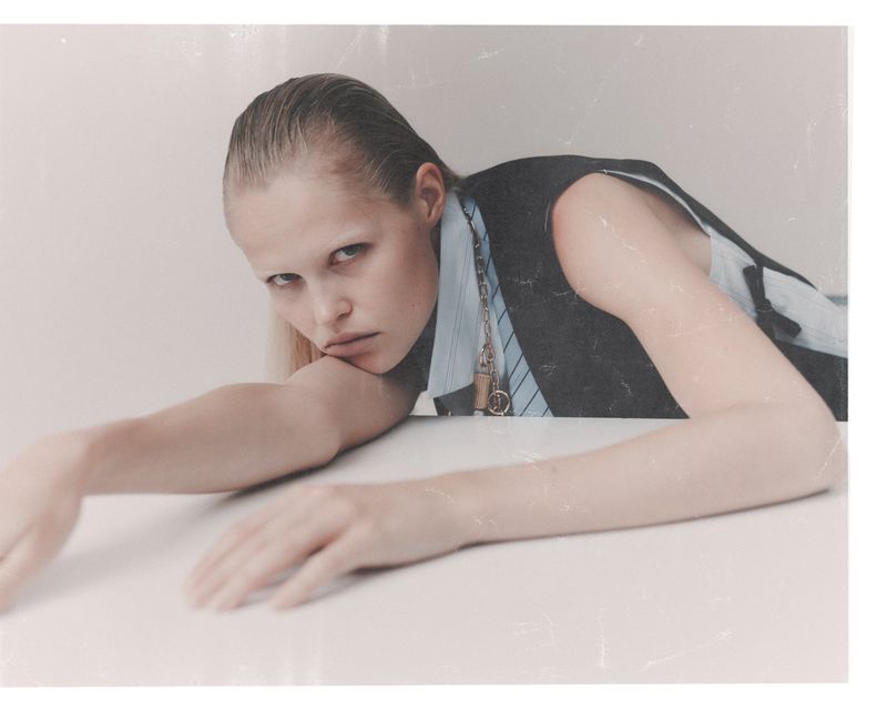 Model Roos Schreiner leaning over a white table wearing a dark vest and striped shirt for WRPD Magazine