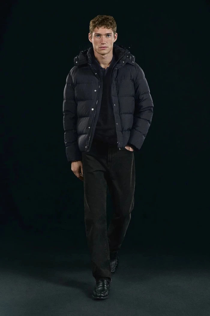 Valentin Humbroich wearing a black puffer jacket and dark trousers against a dark background for Massimo Dutti.