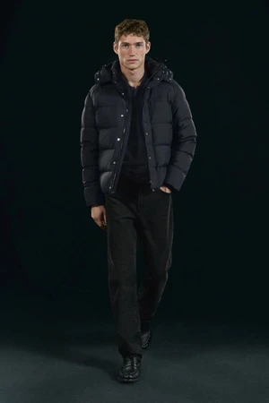 Valentin Humbroich wearing a black puffer jacket and dark trousers against a dark background for Massimo Dutti.