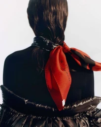 Rear view of a person wearing a black top and red patterned silk scarf tied around dark hair against a plain background