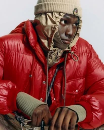 Model wearing a bright red puffer jacket and tan beanie against a plain white background