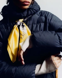 Close-up portrait of a model wearing a dark puffer jacket and a bright yellow patterned silk scarf