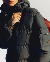 Model wearing a dark puffer jacket with a hood and a red backpack against a plain background