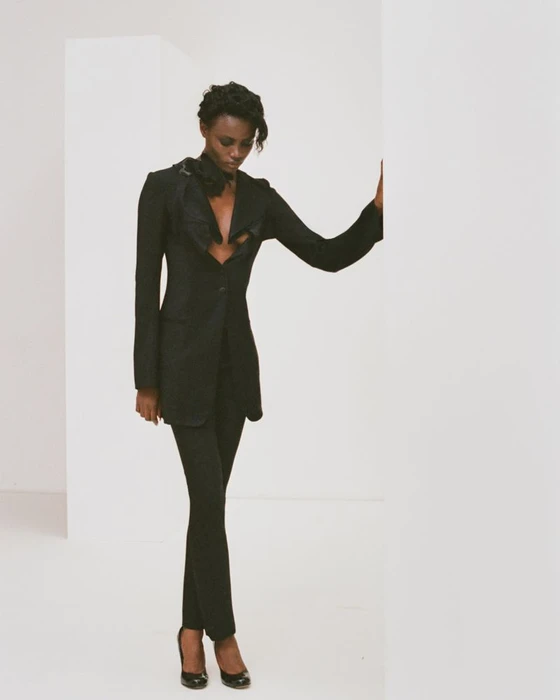 Janet Jumbo wearing a black blazer and matching trousers against a white studio background