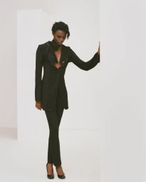 Janet Jumbo wearing a black blazer and matching trousers against a white studio background