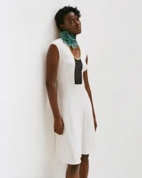 Model Janet Jumbo wearing a white dress with black panel and green neck accessory against white studio backdrop