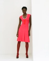Janet Jumbo in a bright pink dress with matching tights and heels standing against a white studio background.
