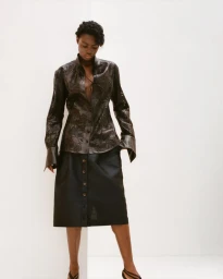 Model Janet Jumbo wearing patterned dark blouse and skirt against a white background for EWUSIE S/S 27 Lookbook