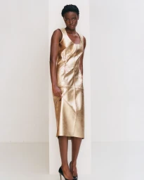 Model Janet Jumbo wearing a shiny gold sleeveless dress against a plain white studio background.