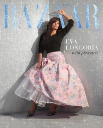 Eva Longoria leaning against a sparkling silver textured background in a black top and a pink floral skirt