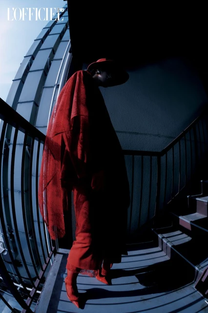 Fashion portrait of a person in red hat and dress standing on a staircase with metal railing, shot with a fisheye lens.