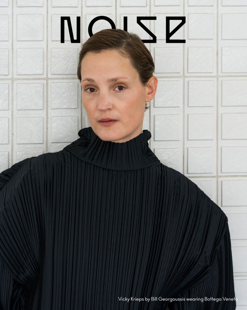 Vicky Krieps wearing a black pleated high-neck top against white tiled background for Beyond Noise Issue 6
