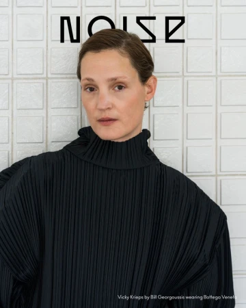 Vicky Krieps wearing a black pleated high-neck top against white tiled background for Beyond Noise Issue 6