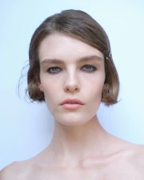 Close-up portrait of a woman with short brown hair and dark eyeliner against a plain light background for Paloma Wool S/S 27