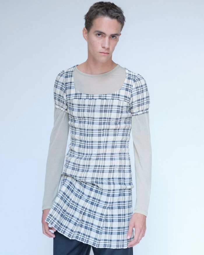 Model in plaid top and skirt over a sheer long-sleeve layer against a pale studio backdrop