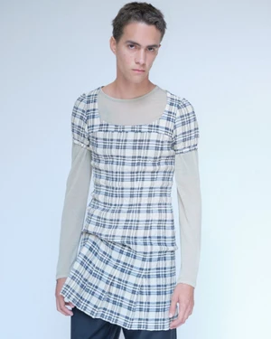 Model in plaid top and skirt over a sheer long-sleeve layer against a pale studio backdrop