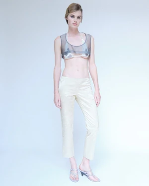 Full-length portrait of a model wearing a sheer grey crop top and light beige trousers against a pale background