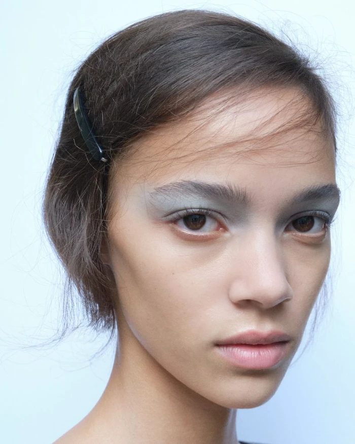 Close-up portrait of a model with grey eyeshadow and a dark hair clip against a light background for Paloma Wool S/S 27