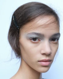 Close-up portrait of a model with grey eyeshadow and a dark hair clip against a light background for Paloma Wool S/S 27