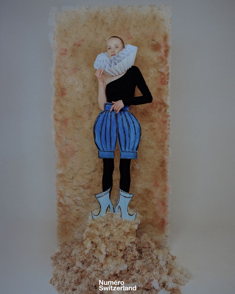 Surreal fashion portrait of a fair-skinned adult woman in a black top and cartoonish blue pants and shoes, in a studio setting.