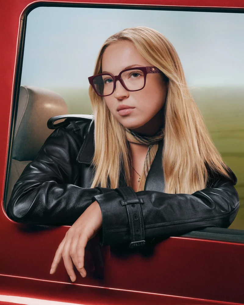 Blonde woman wearing dark glasses and black leather jacket leaning on a red car window