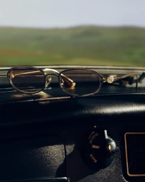 Burberry sunglasses resting on a dark car dashboard with a blurred landscape visible through the windshield.