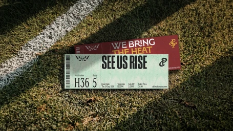 Two event tickets reading SEE US RISE and WE BRING THE HEAT resting on a green turf field with a white line.