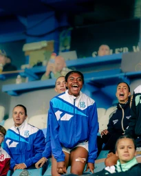 Smiling female athlete in blue and white jacket cheering in stadium stands with teammates