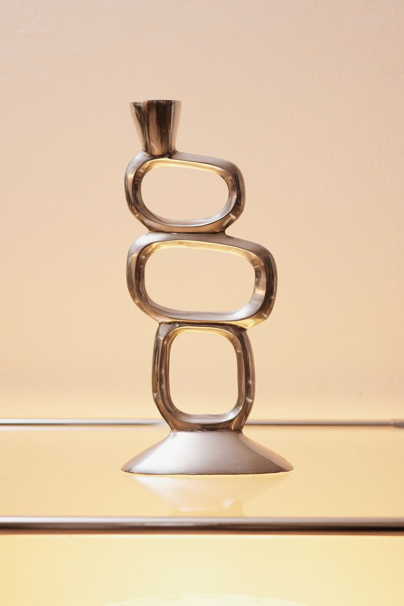 Modern metallic candlestick featuring a geometric design of stacked rounded rectangles, set against a neutral background and reflective surface.