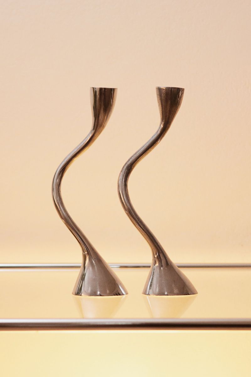 Elegant interior photography featuring a pair of minimalist silver candle holders with curved stems on a reflective surface against a cream backdrop.