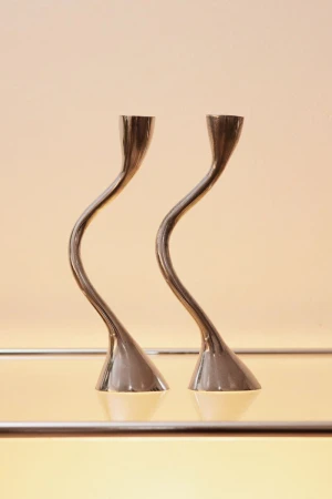 Elegant interior photography featuring a pair of minimalist silver candle holders with curved stems on a reflective surface against a cream backdrop.