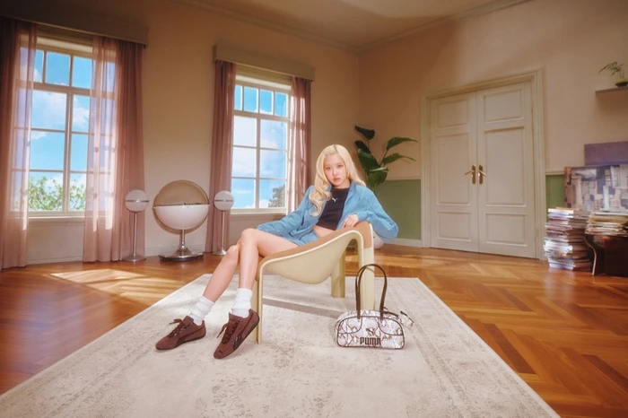 ROSÉ seated in a modernist chair wearing a blue jacket and brown sneakers for the Puma Speedcat Croc campaign.