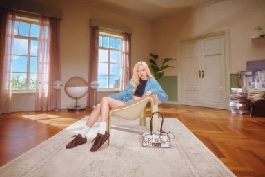 ROSÉ seated in a modernist chair wearing a blue jacket and brown sneakers for the Puma Speedcat Croc campaign.