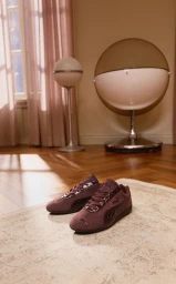 Puma Speedcat Croc sneakers in brown resting on a light-colored rug in a mid-century modern interior setting.
