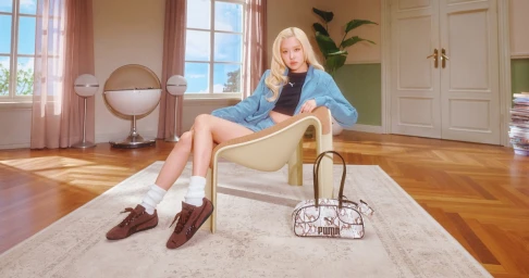 ROSÉ seated in a modern armchair wearing a blue jacket and brown sneakers with a Puma handbag on the floor