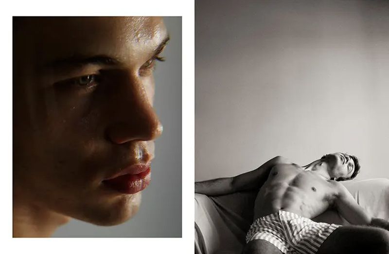 Close up portrait of shirtless male model with wet skin and striped boxer shorts reclining on a sofa in a dimly lit studio.