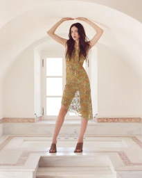 Model standing inside an arched room with both hands pressed against the curved ceiling wearing a patterned slip dress.