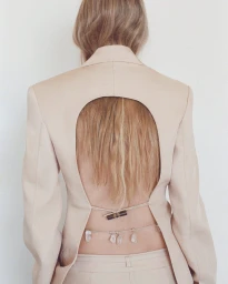 Rear view of a woman wearing a beige blazer with a large oval cut-out revealing her lower back and crystal body chain.