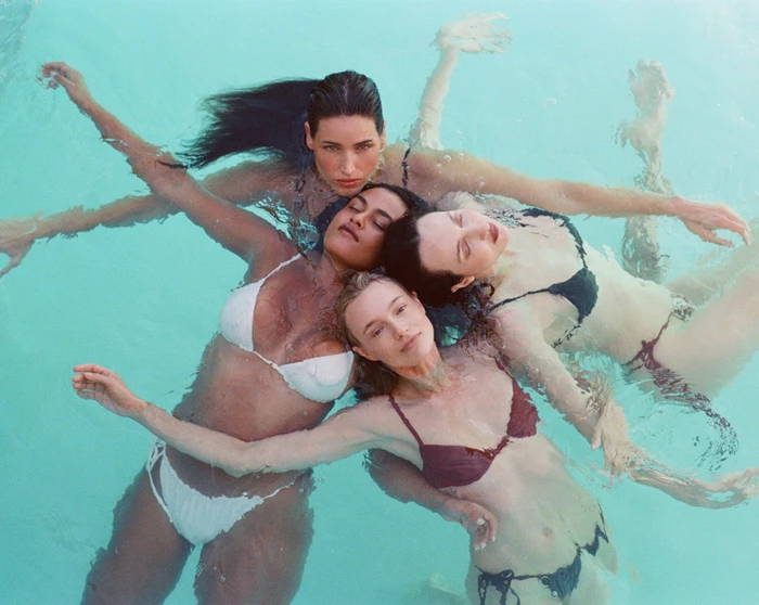 Four women floating on their backs in a turquoise swimming pool, arranged in a circular formation.