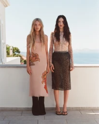 Two models standing on a sunny balcony overlooking the sea, wearing designer fashion pieces for the SIR. Resort 2027 campaign.