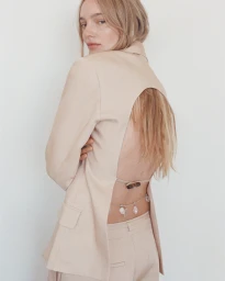 Model wearing a beige cutout blazer looking over her shoulder against a plain white wall