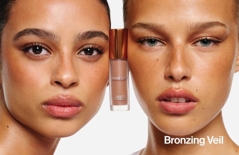 Two models showcasing a bronzing product bottle held between their faces against a white background for Haus Labs